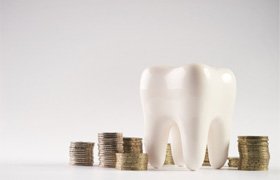 A closeup of a white healthy human tooth model and stacked coins 
