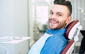 Man in denim jacket sitting in dental chair and smiling