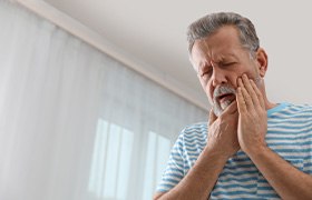 Older bearded man rubbing his jaw and looking concerned