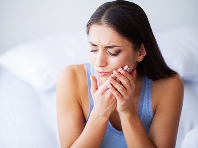 Woman rubbing jaw in pain needing dental implant salvage in Beverly, MA