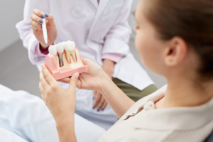 Close up of dentist pointing at dental implant model that patient is holding