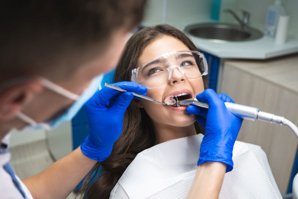 Dentist in blue gloves performing root canal on woman with dark hair